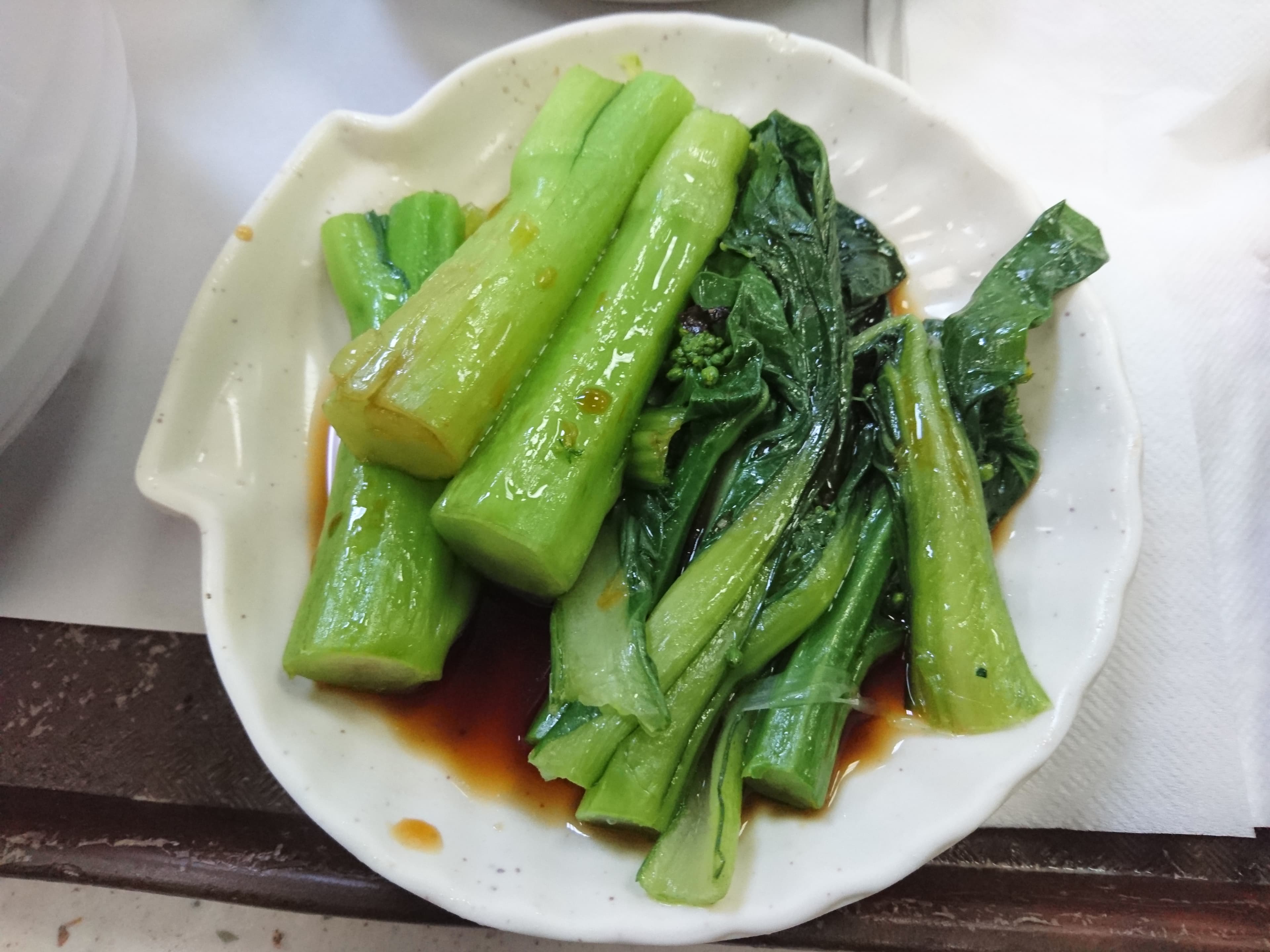 Cooked choy sum served with soy sauce on a white plate