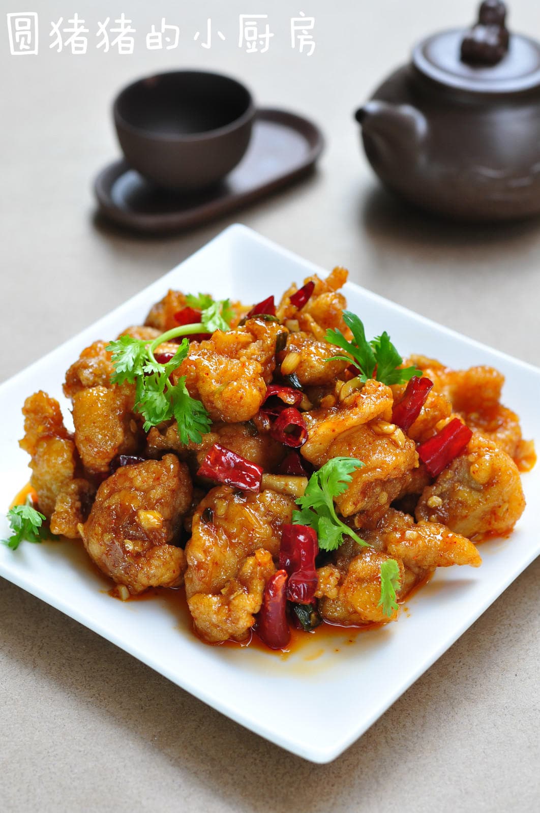 General Tso's chicken with a glossy sauce, dried red chilies and cilantro on a white plate, with the original creator watermark.