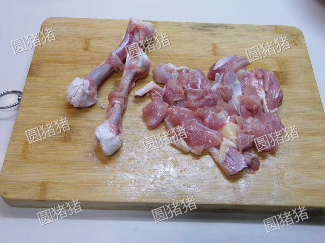 Raw chicken leg meat cut into pieces beside the removed bones on a wooden board.