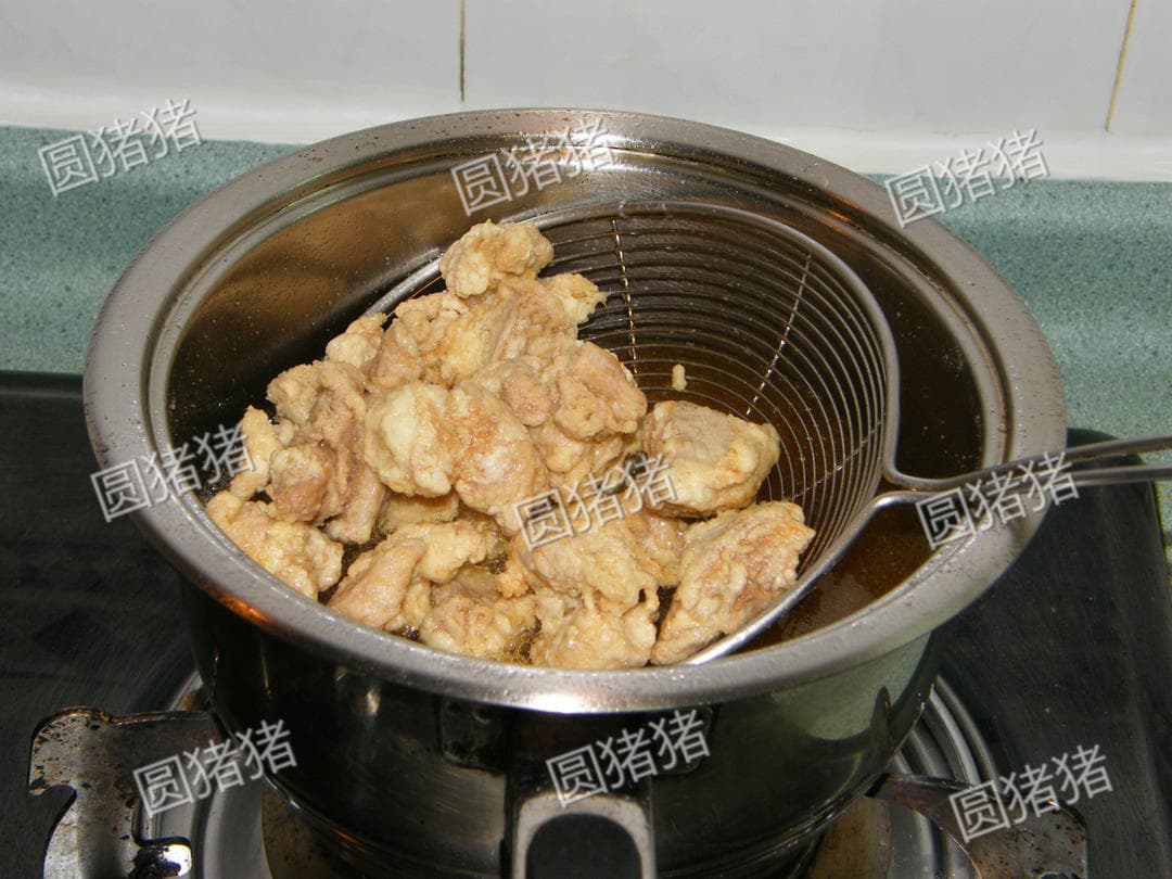 Fried coated chicken pieces lifted above a pot in a wire skimmer to drain.