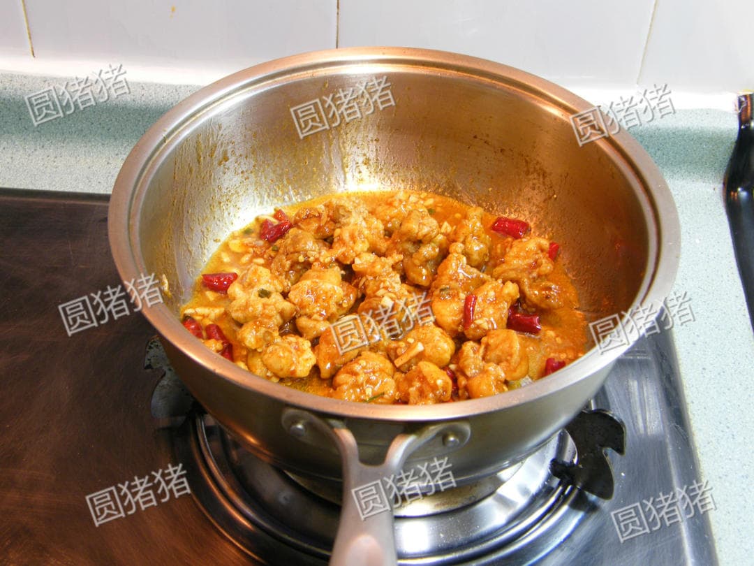 Fried chicken pieces coated with glossy chili sauce in the skillet after tossing.