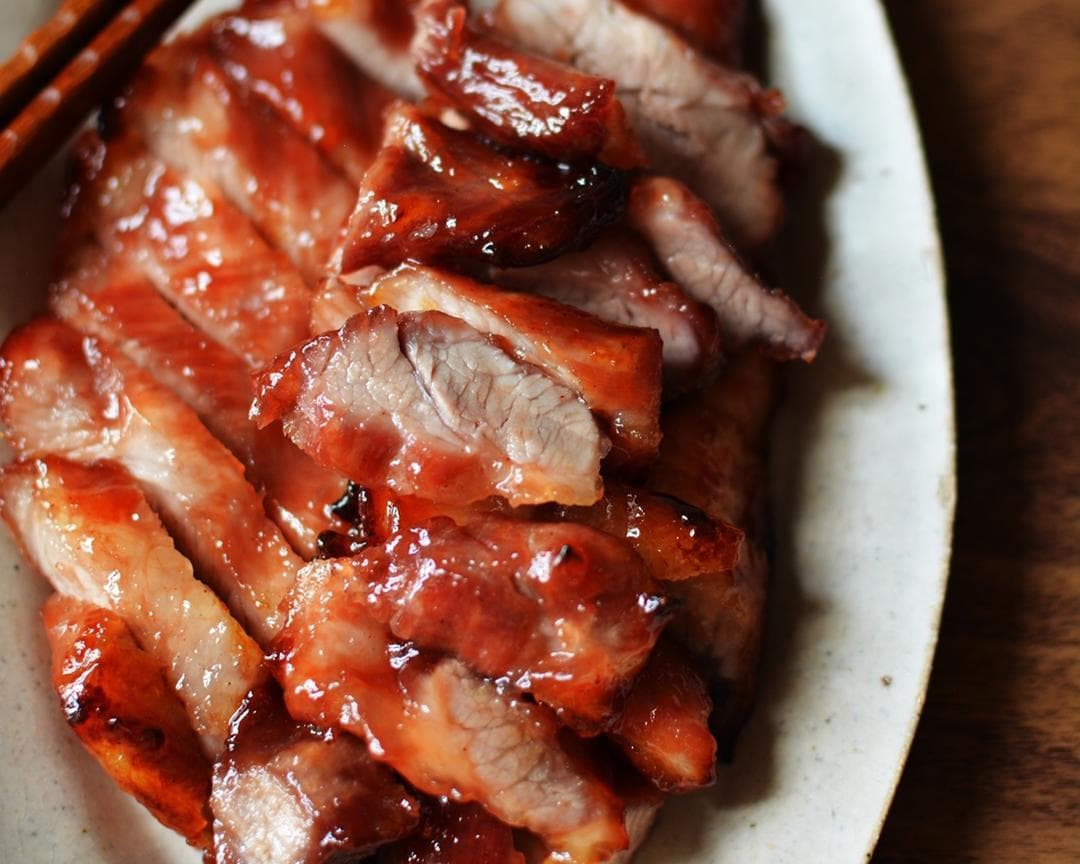 Sliced Cantonese char siu pork with a glossy reddish glaze arranged on a white plate.