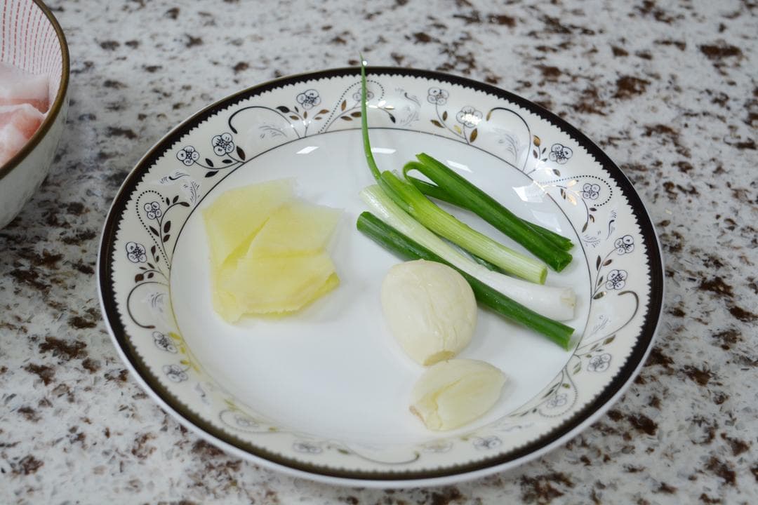 Sliced ginger, short scallion lengths and garlic cloves arranged on a small white plate.