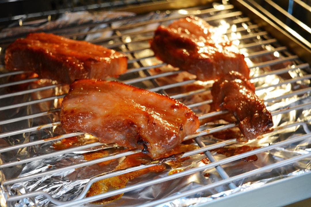 Glazed pork pieces roasting on a wire rack above a foil-lined drip tray.