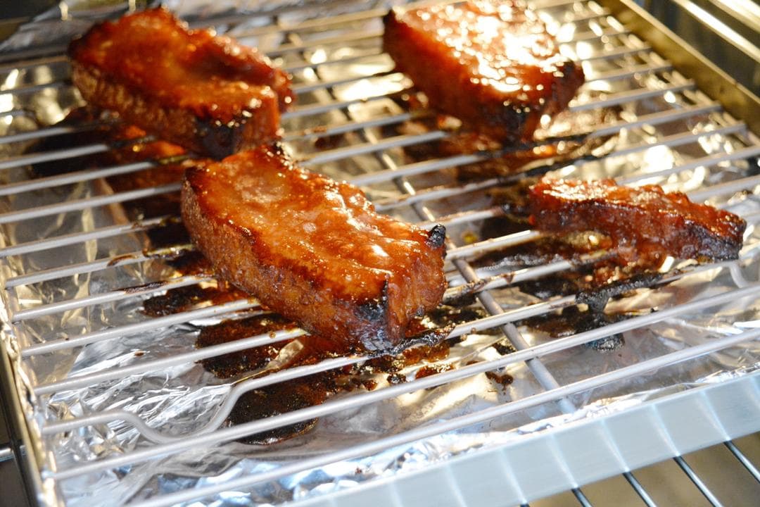 Later-stage roasted pork pieces with darker glazed edges on the same wire rack and foil-lined tray.