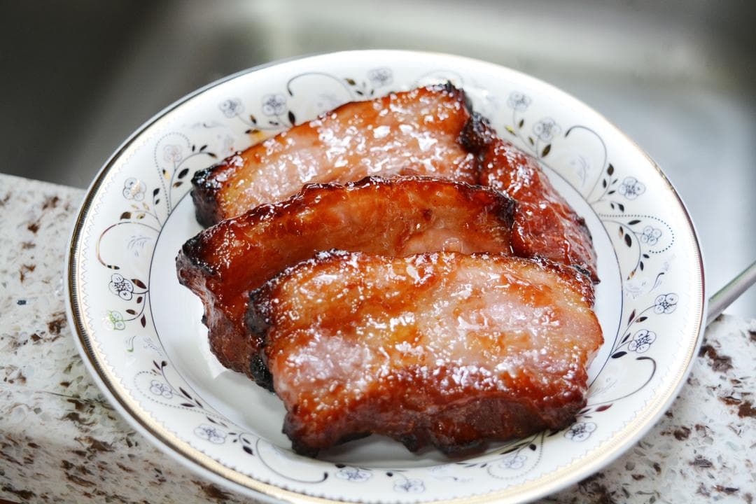 Finished honey-glazed pork pieces on a patterned white plate before slicing.