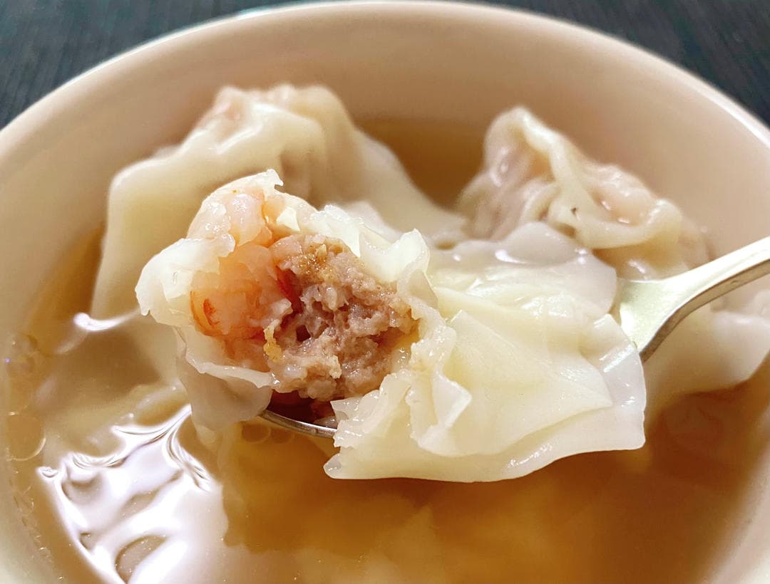A Cantonese pork and shrimp wonton opened on a spoon above a bowl of clear soup.