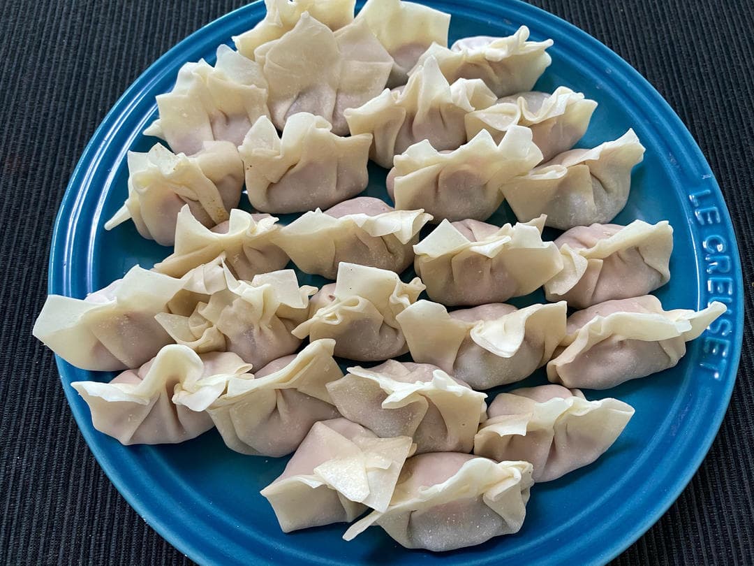 Freshly wrapped uncooked pork and shrimp wontons arranged on a blue plate.