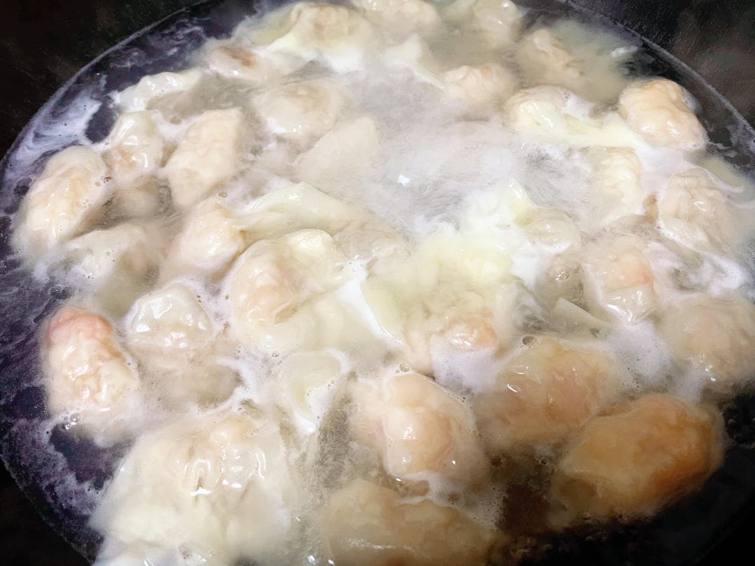 Wontons cooking in a pot of water with bubbles around their thin wrappers.
