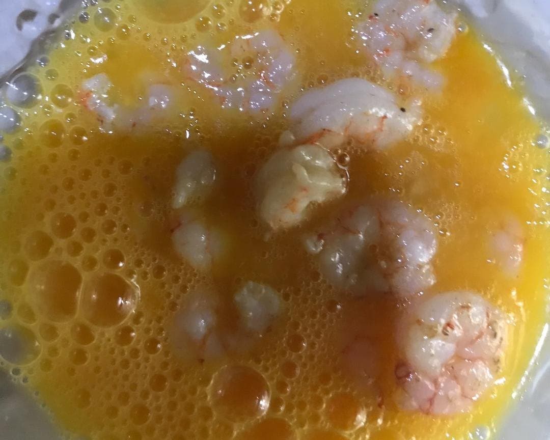 Cooked shrimp mixed into beaten egg before the final gentle pan cook.