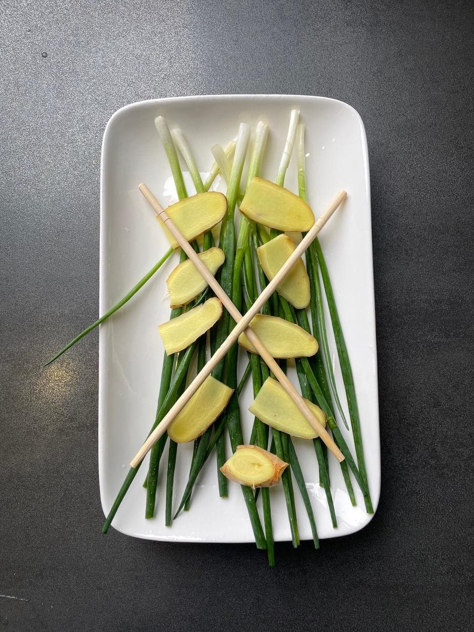 Ginger slices, scallion sections and plain chopsticks arranged on a plate to support the fish.
