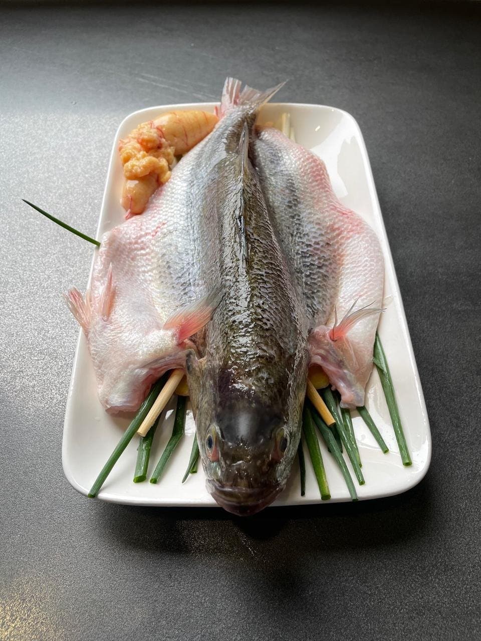 An opened whole fish resting on the ginger-scallion bed before steaming.