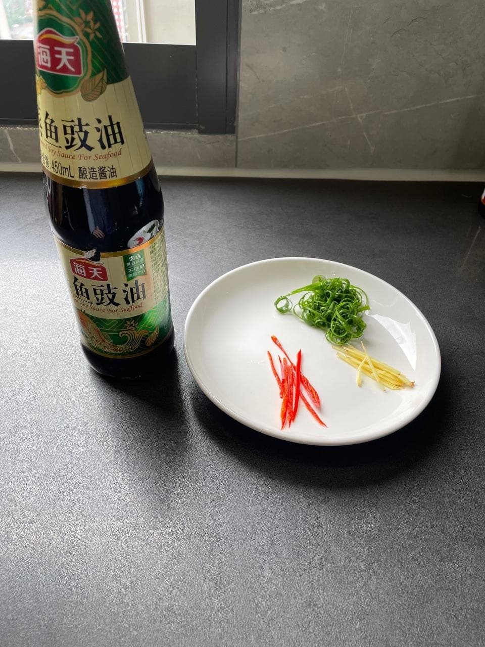 Shredded scallion, ginger and red chili beside a bottle labeled seasoned soy sauce for seafood.