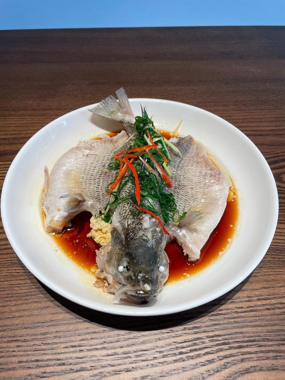 Finished steamed whole fish with ginger, scallion and red pepper shreds above the soy sauce.