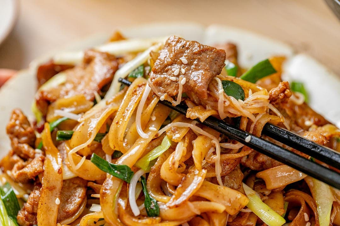 Cantonese beef chow fun with wide rice noodles, sliced beef, bean sprouts, scallion greens and sesame seeds.