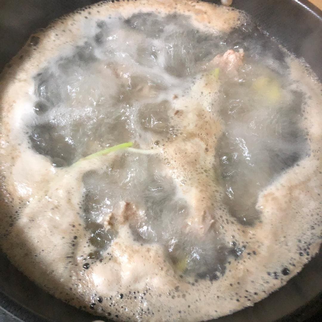 Pork ribs blanching with scallion as foam rises to the water surface.