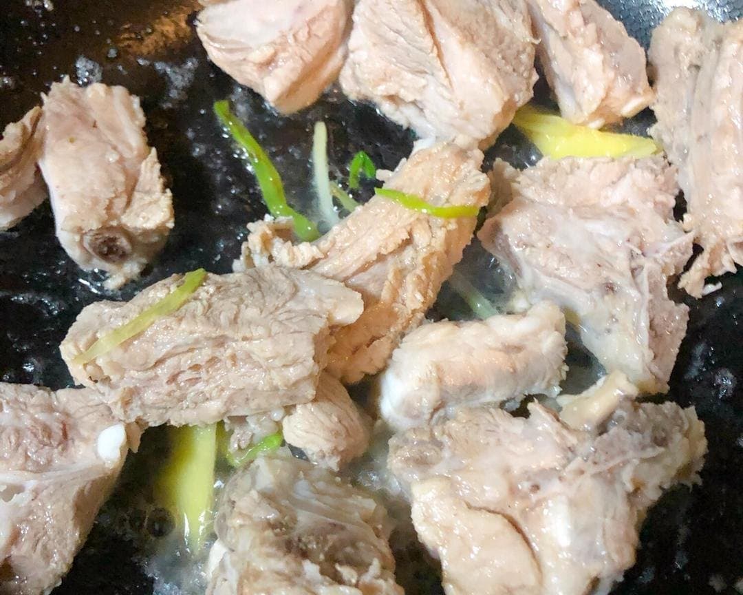 Blanched ribs being turned in a pan with ginger and scallion.